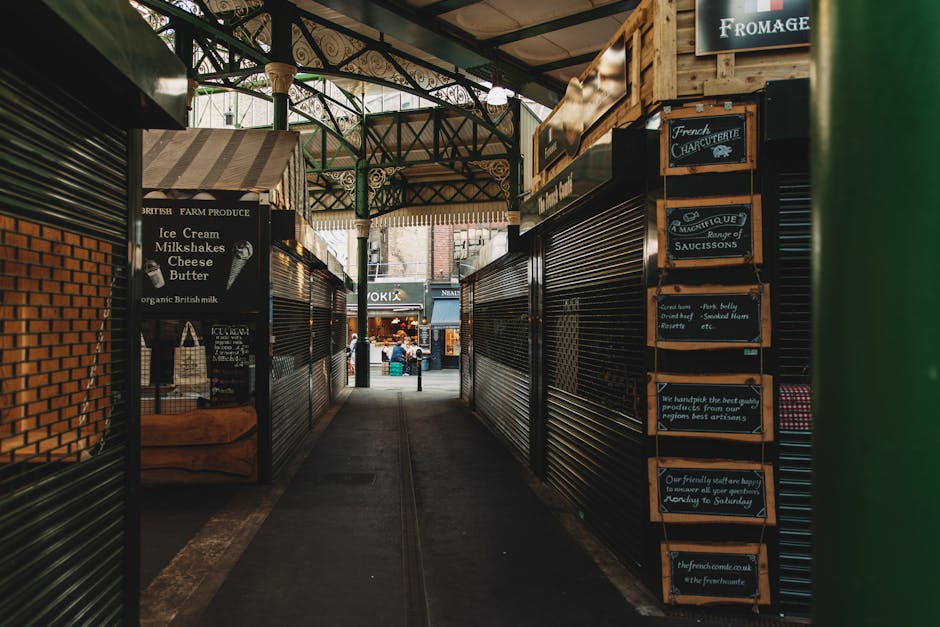 Inside a large industrial market hall, featuring blue steel support columns and bright overhead lighting, with numerous vendors and shoppers browsing tables filled with an array of jewelry, accessorie